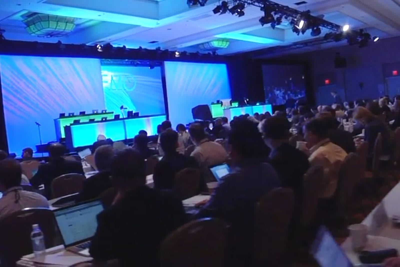 The DEMO conference stage in a hotel ballroom, the audience working on laptops at long tables (mid-2000s; frame from DEMO's event video)